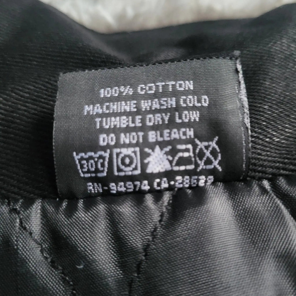 Étiquette d’un vêtement noir 100% coton, marque et taille non visibles. Fripes Sélect