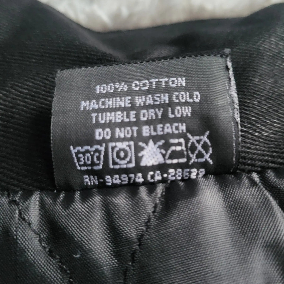 Étiquette d’un vêtement noir 100% coton, marque et taille non visibles. Fripes Sélect