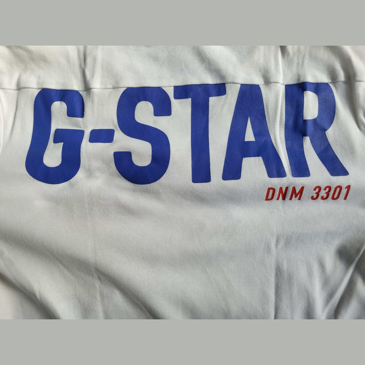 T-shirt blanc G-Star, logo bleu, inscription DNM 3301, taille non visible. Fripes Sélect