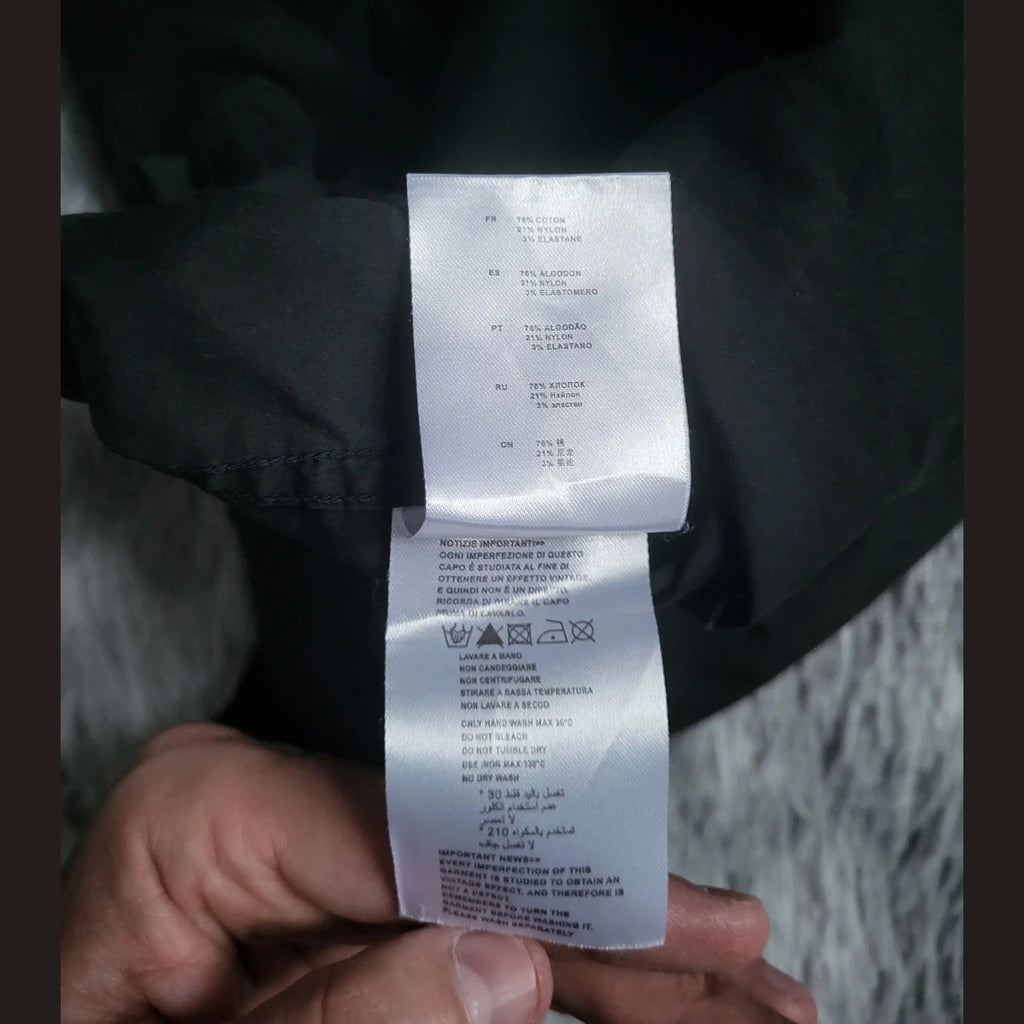 Étiquette d’un vêtement noir, marque et taille non visibles, composition coton. Fripes Sélect