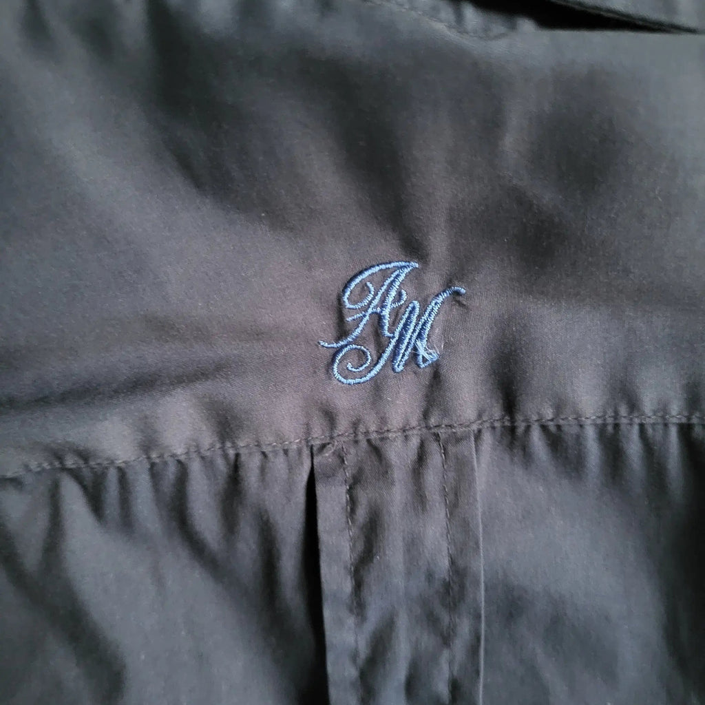 Chemise noire, initiales brodées AM en bleu, taille non visible. Fripes Sélect