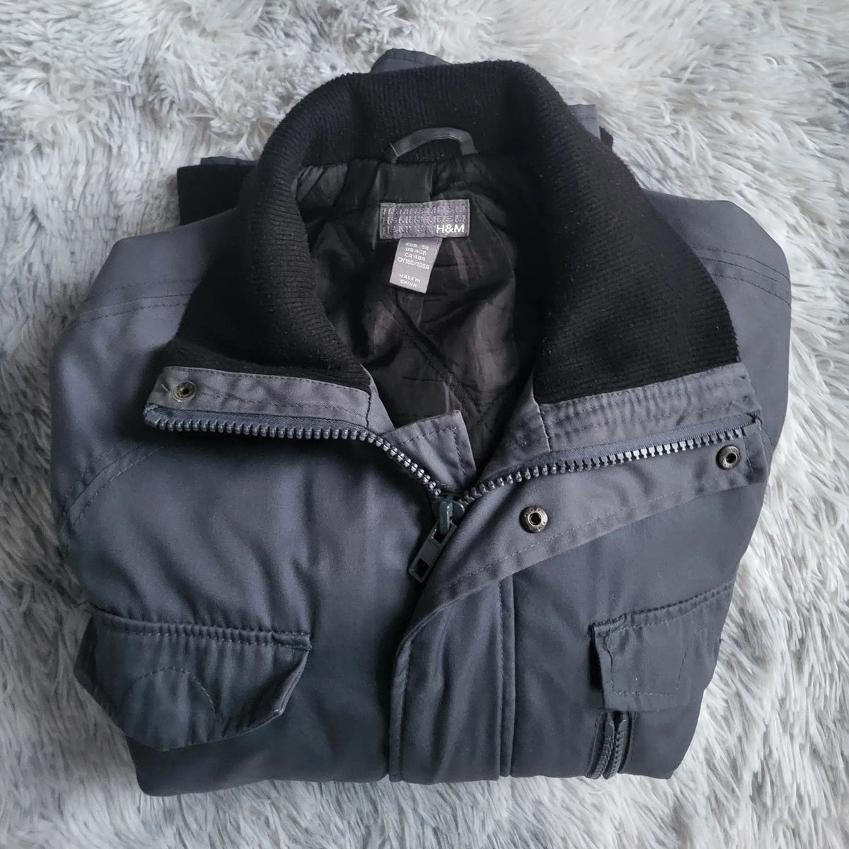 Veste noire H&M, taille L, posée sur une couverture grise. Fripes Sélect