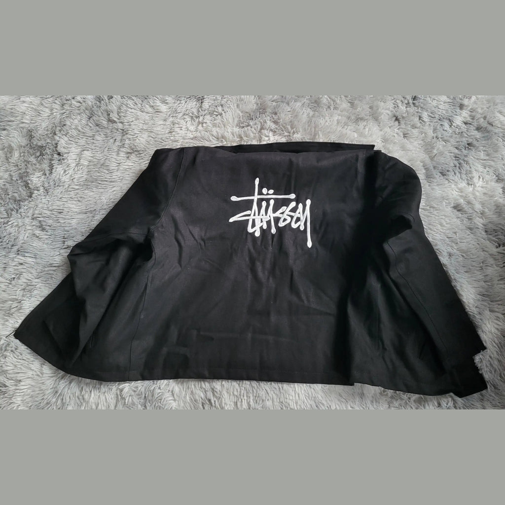 Veste noire Stüssy, logo blanc au dos, taille non visible. Fripes Sélect