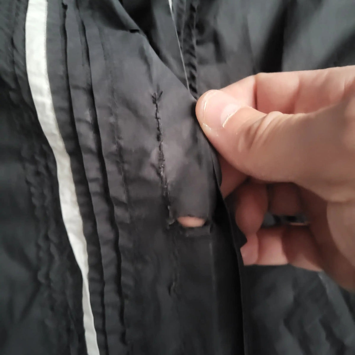 Veste noire à bande blanche, trou visible, marque et taille non indiquées. Fripes Sélect