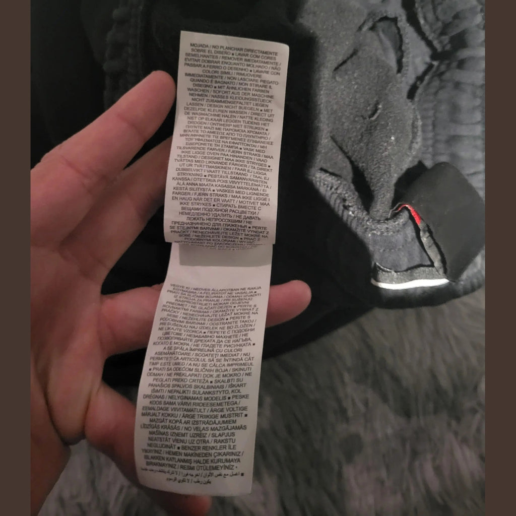 Étiquette d’un vêtement noir, marque et taille non visibles, Fripes Sélect