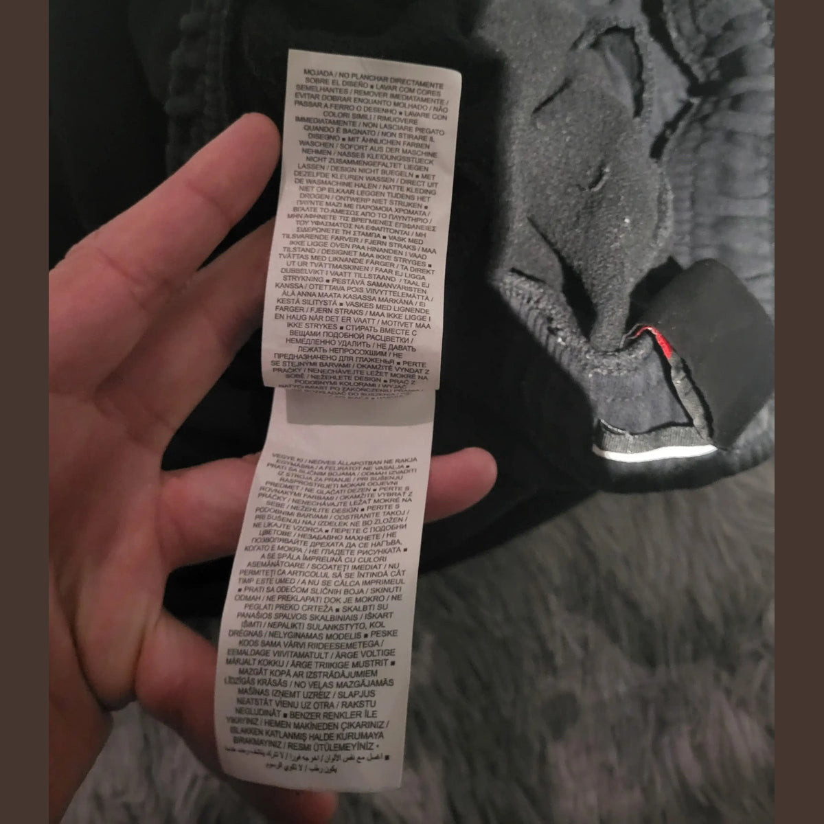 Étiquette d’un vêtement noir, marque et taille non visibles, Fripes Sélect