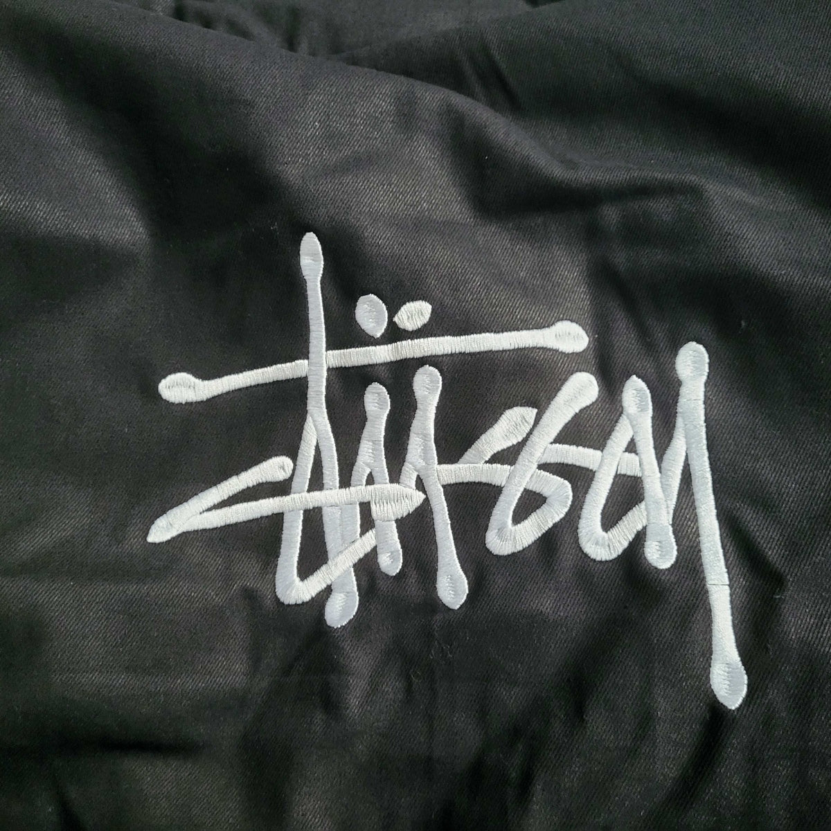 Veste noire Stüssy, logo brodé blanc, taille non visible. Fripes Sélect